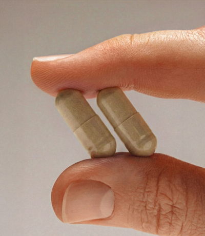 Hand holding two VIVID Recovery capsules — NAC, milk thistle, ginger and vitamin B1 hangover support supplement.