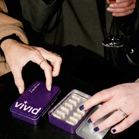 Friends holding drinks and a VIVID Recovery hangover support tin after a night out.